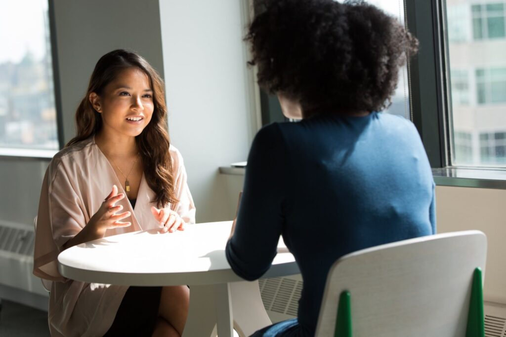 Two women converse at a desk.