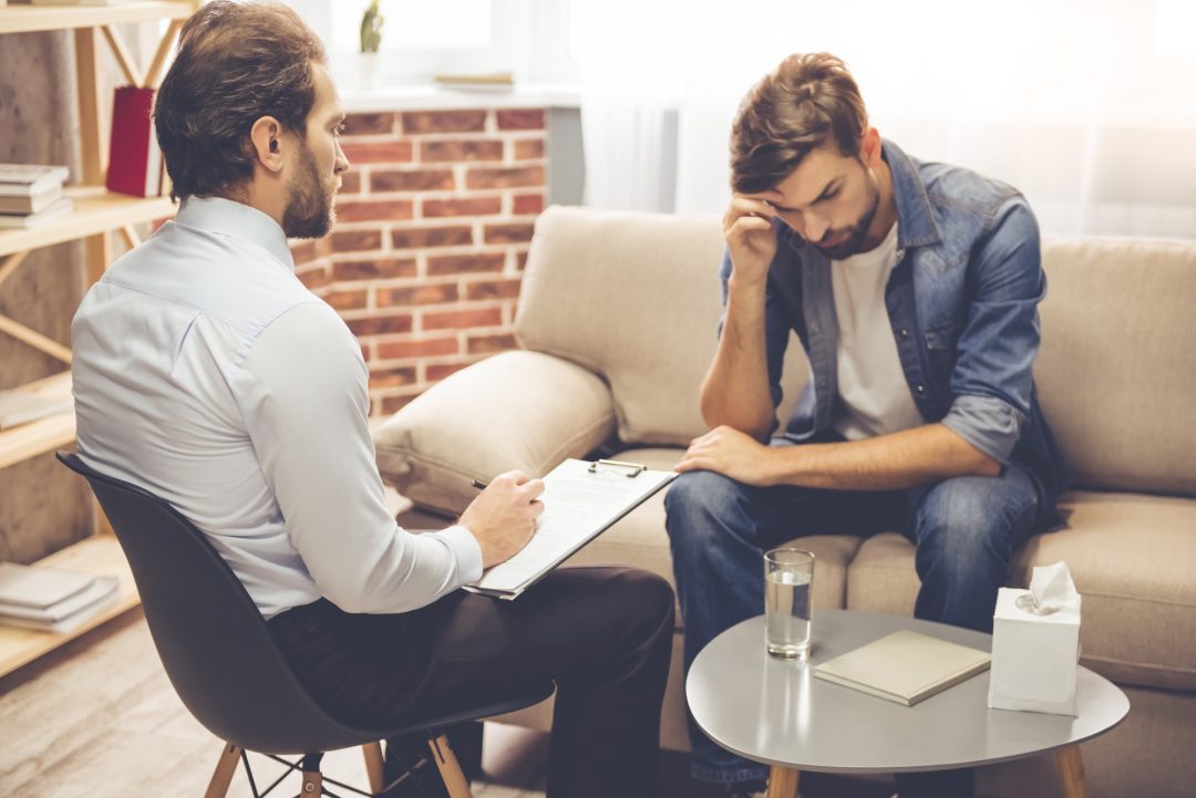 Two men converse while sitting on a couch